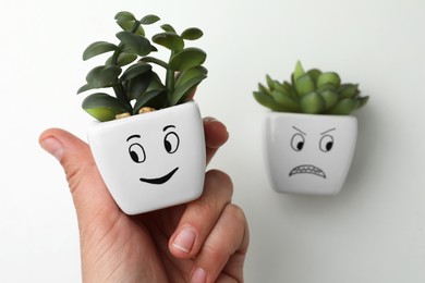 Photo of Woman choosing potted plant with happy face over angry one on white background, closeup. Emotional management