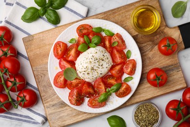 Tasty salad Caprese with mozarella, tomatoes, basil and other ingredients on light table, flat lay