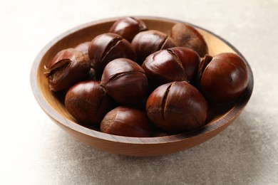 Photo of Fresh edible sweet chestnuts in wooden bowl on grey table