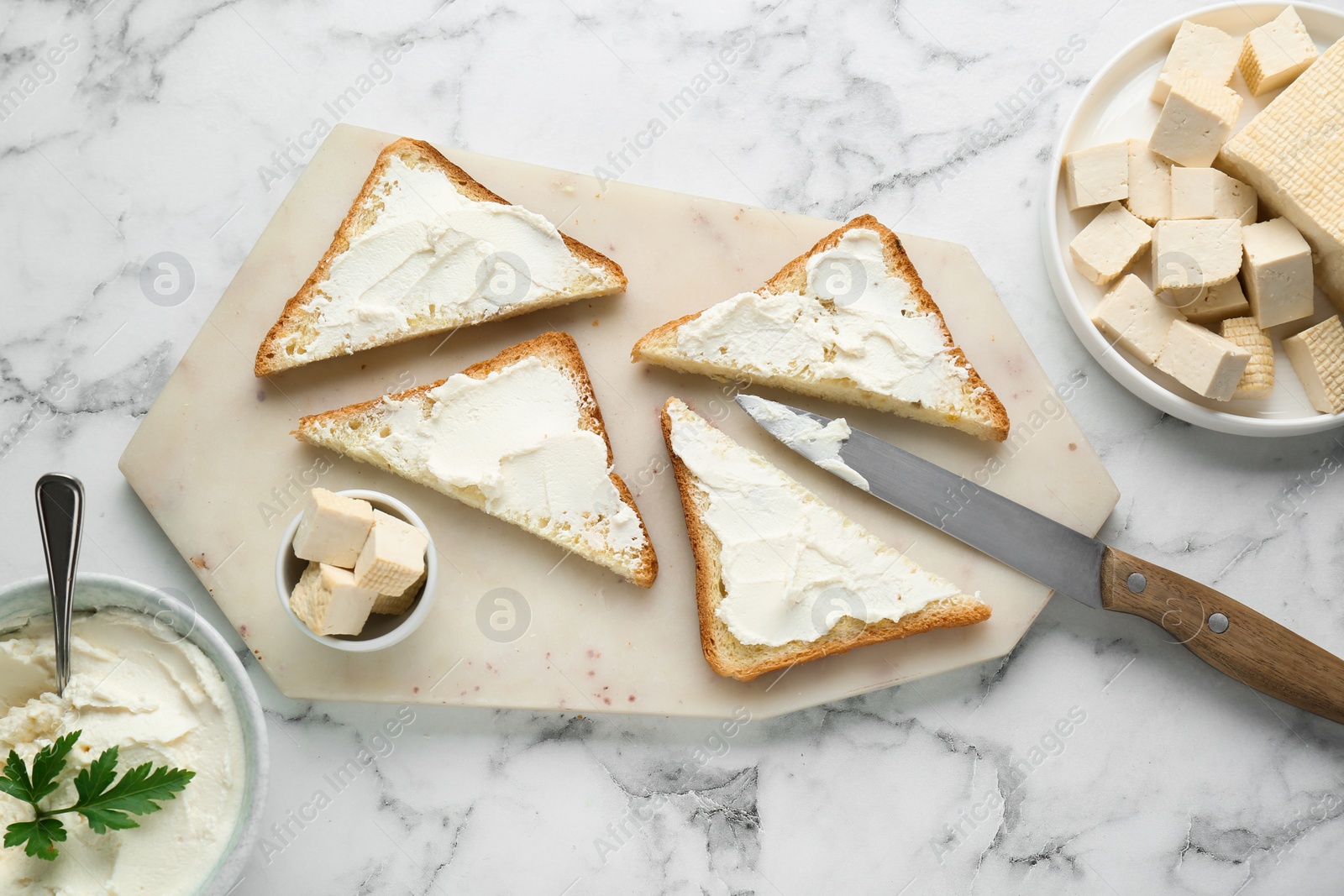 Photo of Delicious toasts with tofu cream cheese and parsley on white marble table, flat lay.