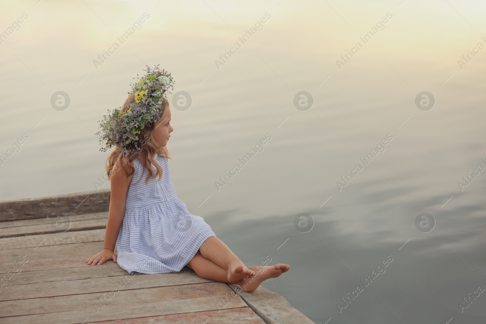 Photo of Cute little girl wearing wreath made of beautiful flowers on pier near river