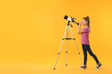 Photo of Cute little girl looking at stars through telescope on orange background, space for text