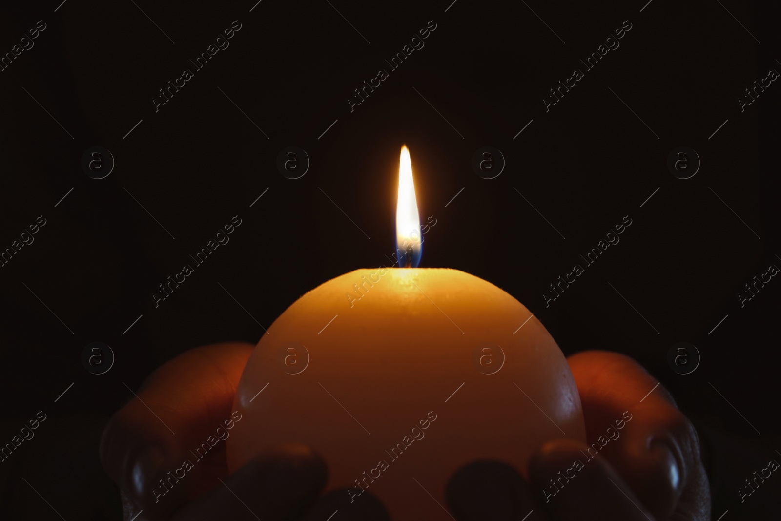 Photo of Young person holding burning candle in darkness, closeup