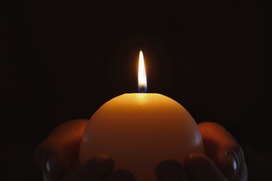 Photo of Young person holding burning candle in darkness, closeup