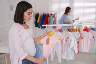 Photo of Happy pregnant woman with shopping bags choosing baby clothes in store