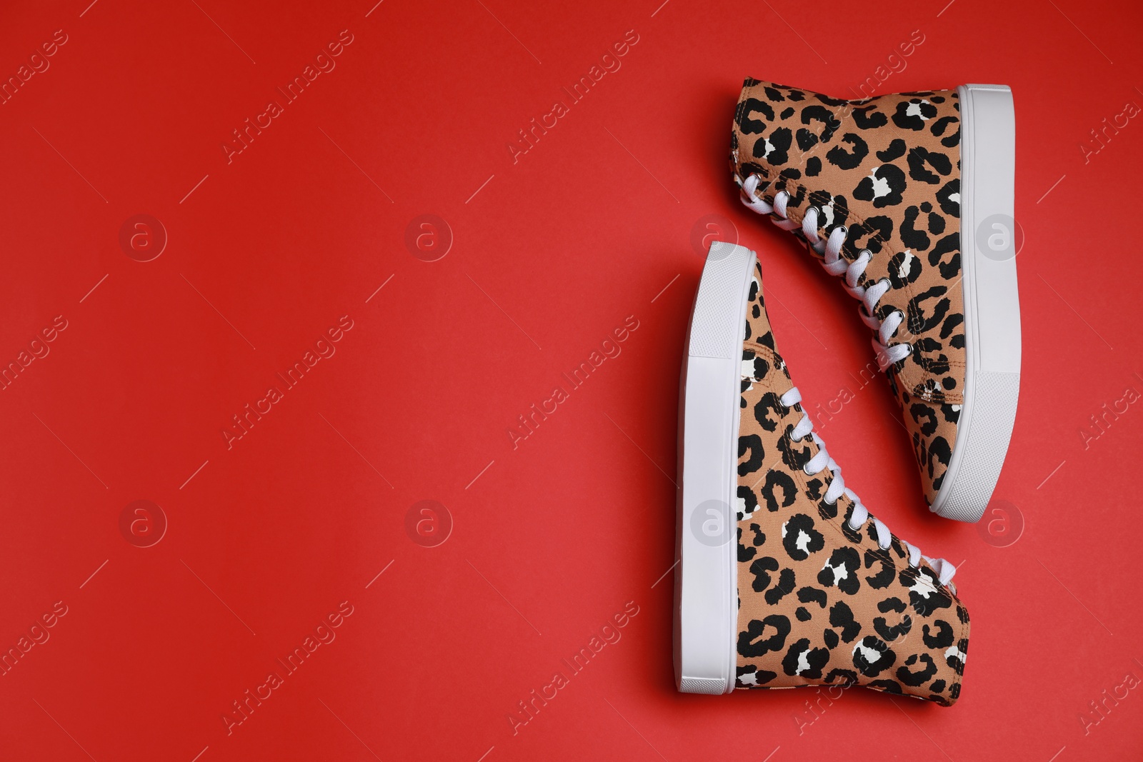 Photo of Pair of classic old school sneakers with leopard print on red background, flat lay. Space for text