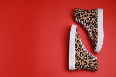 Photo of Pair of classic old school sneakers with leopard print on red background, flat lay. Space for text