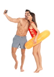 Photo of Young attractive couple in beachwear with inflatable ring taking selfie on white background