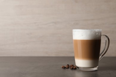 Glass cup of delicious layered coffee and beans on grey table against light background, space for text