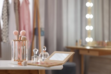 Set of brushes, eyeshadow palette and perfumes on white table in makeup room, space for text