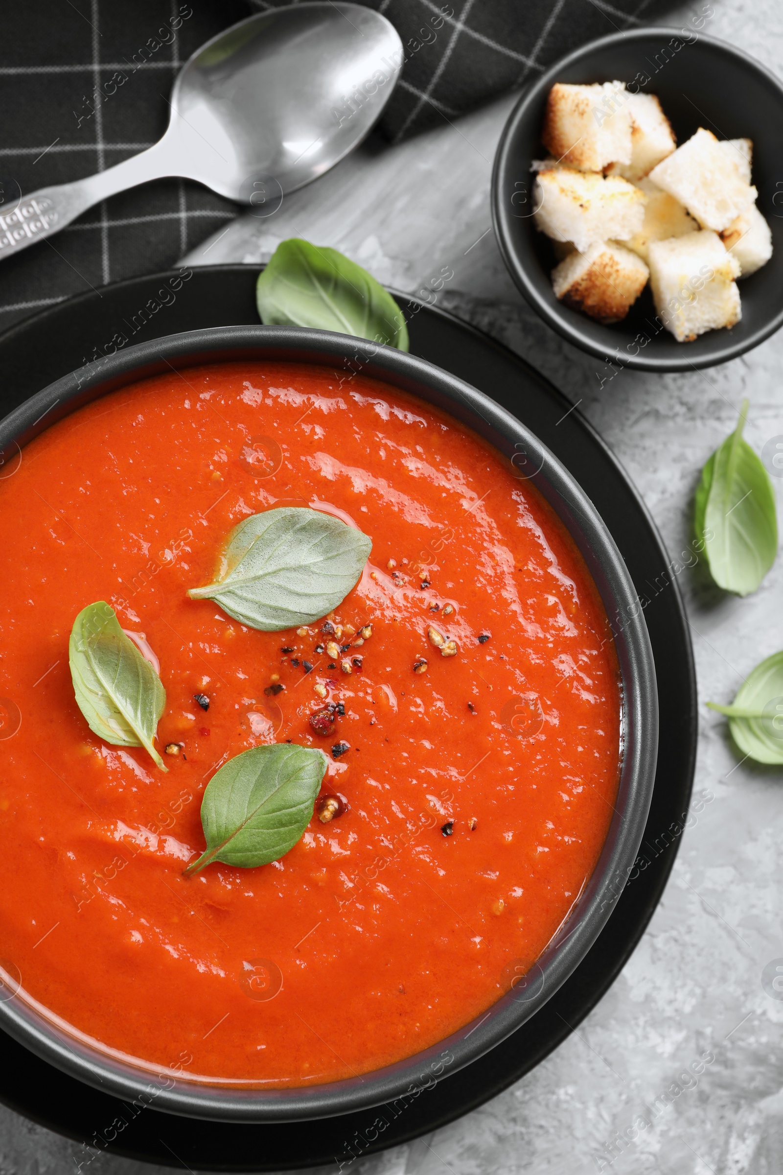 Photo of Delicious tomato cream soup served on grey textured table, flat lay