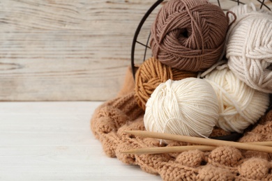 Soft woolen yarns with knitting needles and sweater on white table, closeup. Space for text