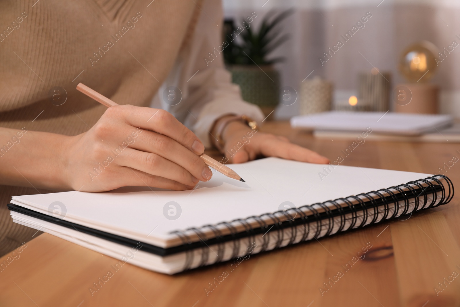 Photo of Woman drawing in sketchbook with pencil at wooden table indoors, closeup