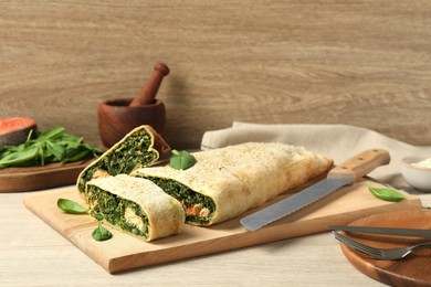 Photo of Delicious strudel with salmon and spinach served on light wooden table