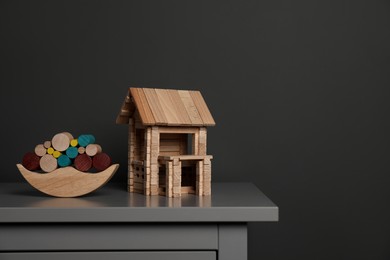 Photo of Wooden balance toy and house on chest of drawers near dark grey wall, space for text. Children's toys
