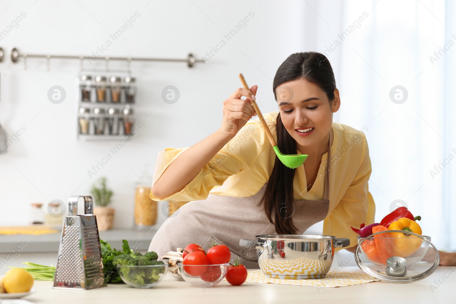 Photo of Young woman tasting delicious soup in kitchen