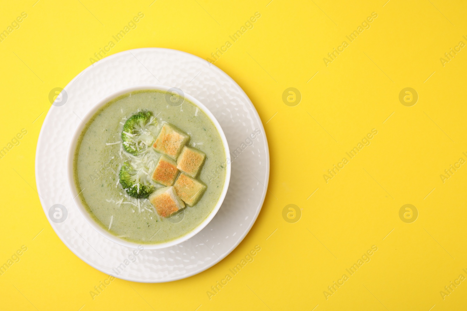 Photo of Delicious broccoli cream soup with croutons and cheese on yellow background, top view. Space for text