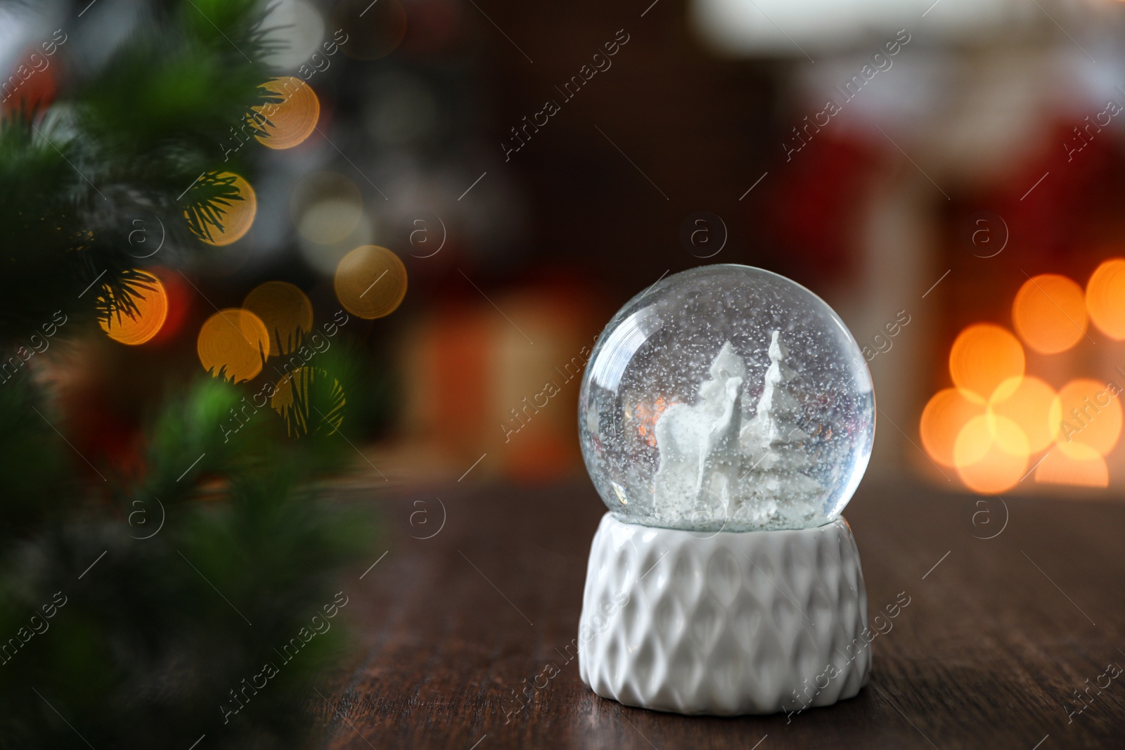 Photo of Snow globe on wooden table against blurred background, space for text. Bokeh effect