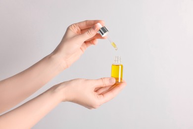 Woman holding bottle of cosmetic oil on light background, closeup