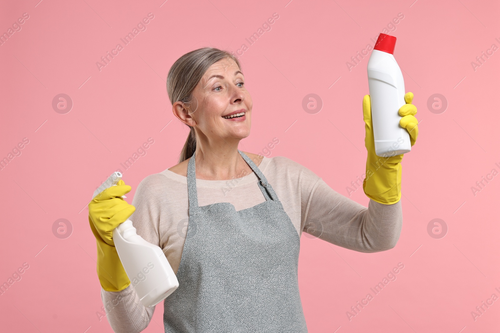 Photo of Happy housewife with bottles of detergent on pink background