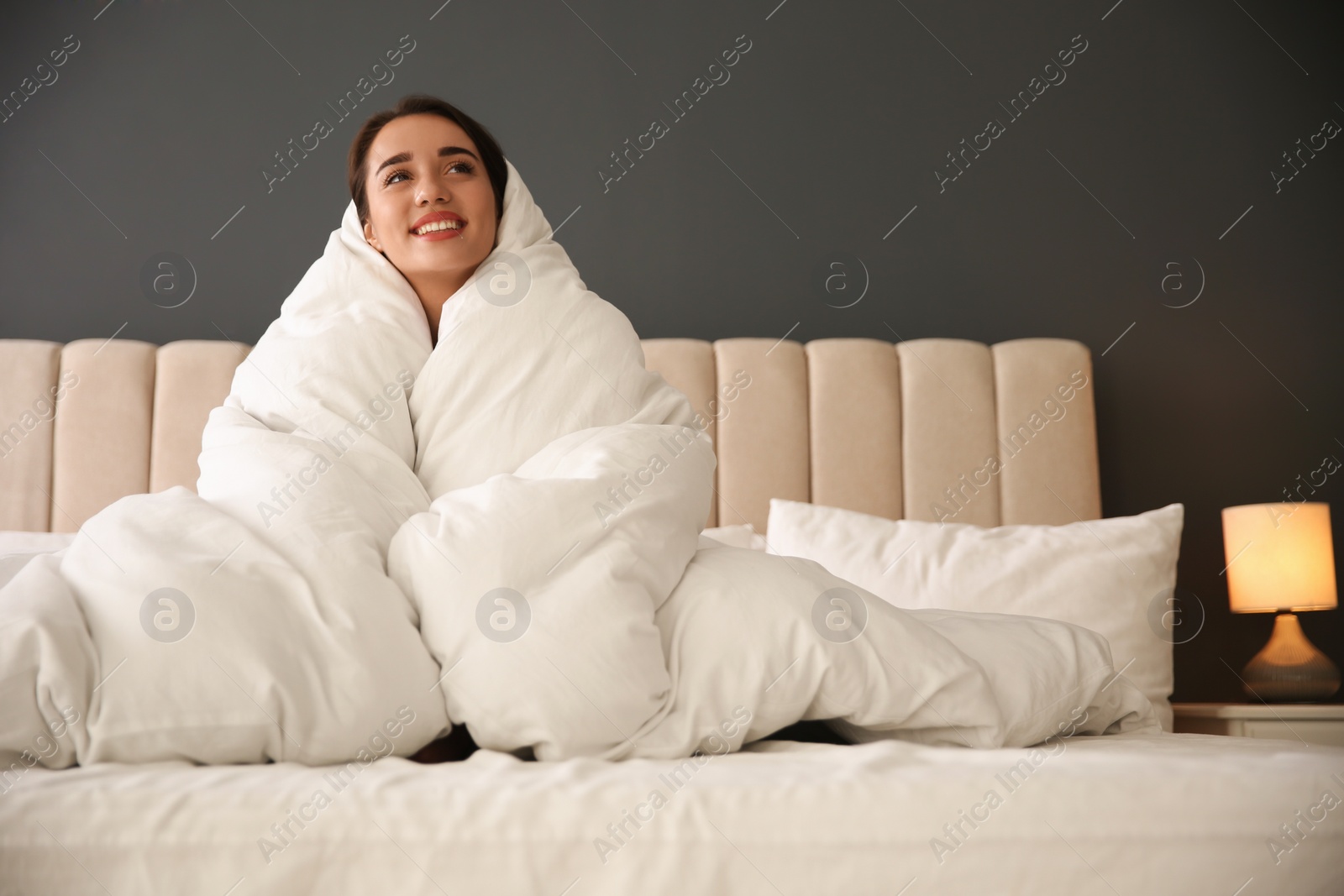 Photo of Beautiful young woman wrapped with soft blanket relaxing on bed at home