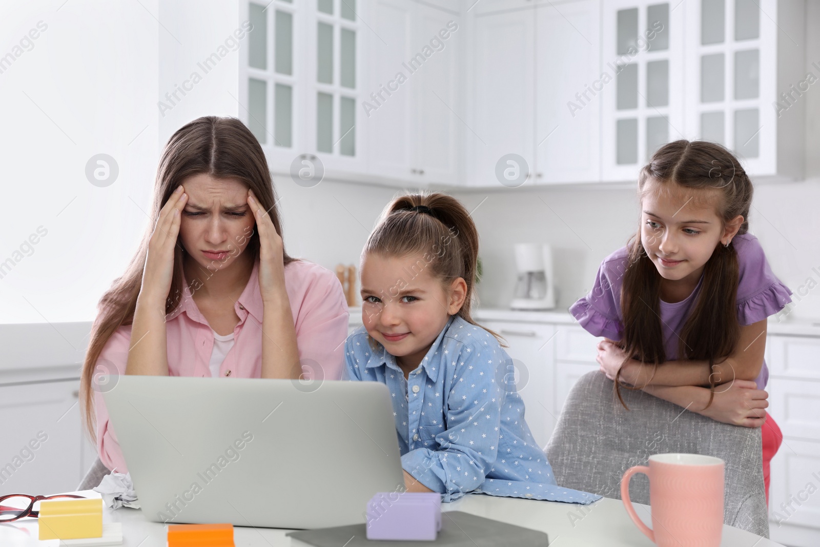 Photo of Children disturbing stressed woman in kitchen. Working from home during quarantine