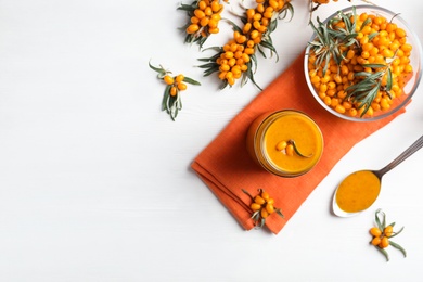 Photo of Delicious sea buckthorn jam and fresh berries on white wooden table, flat lay. Space for text