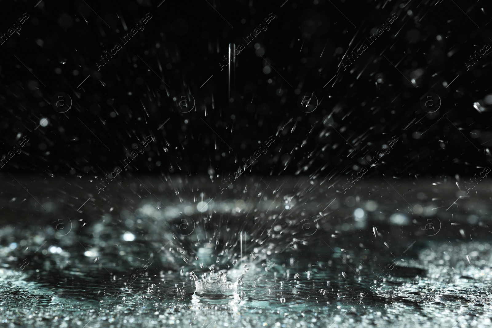 Photo of Rain drop falling down into puddle on dark background