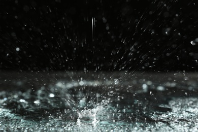 Photo of Rain drop falling down into puddle on dark background