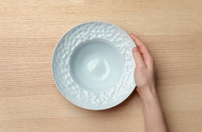 Woman with empty plate at wooden table, top view