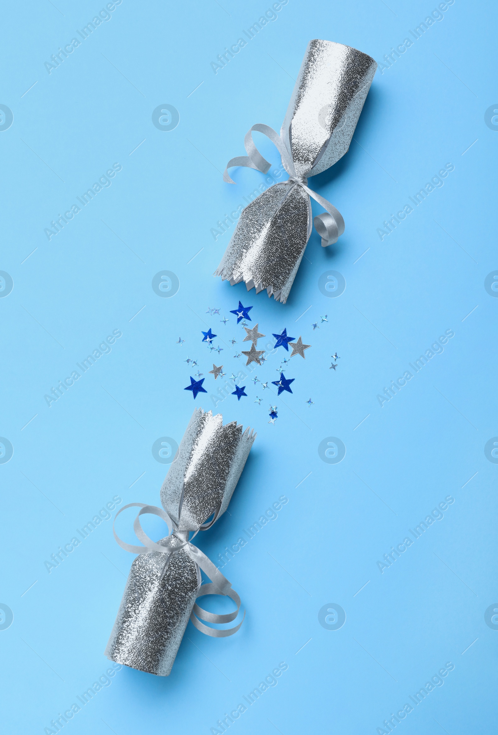 Photo of Open silver Christmas cracker with shiny confetti on light blue background, top view