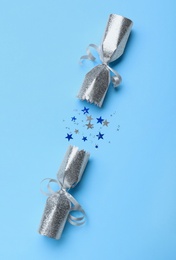 Photo of Open silver Christmas cracker with shiny confetti on light blue background, top view