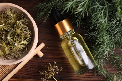 Photo of Bottle of essential oil and fresh dill on wooden table, flat lay