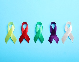 Photo of Colorful ribbons on light blue background, flat lay. World Cancer Day