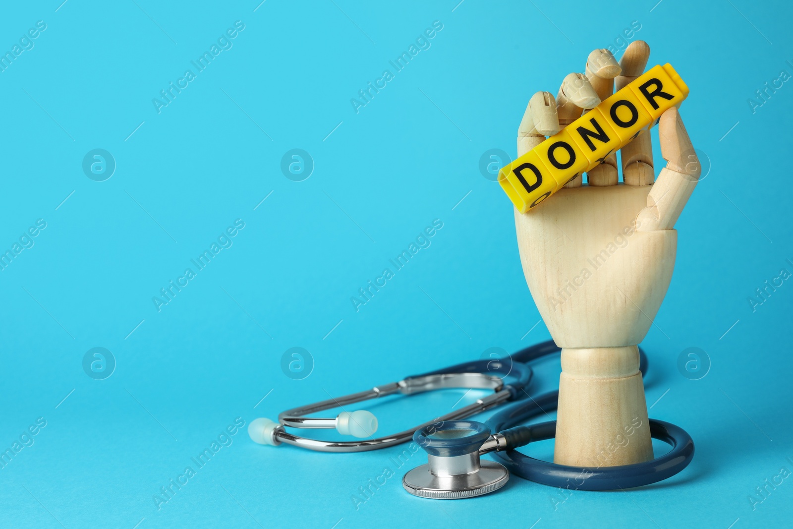 Photo of Mannequin hand holding word Donor made of cubes and stethoscope on light blue background. Space for text
