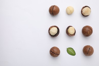 Photo of Tasty Macadamia nuts and green leaf on white background, flat lay. Space for text