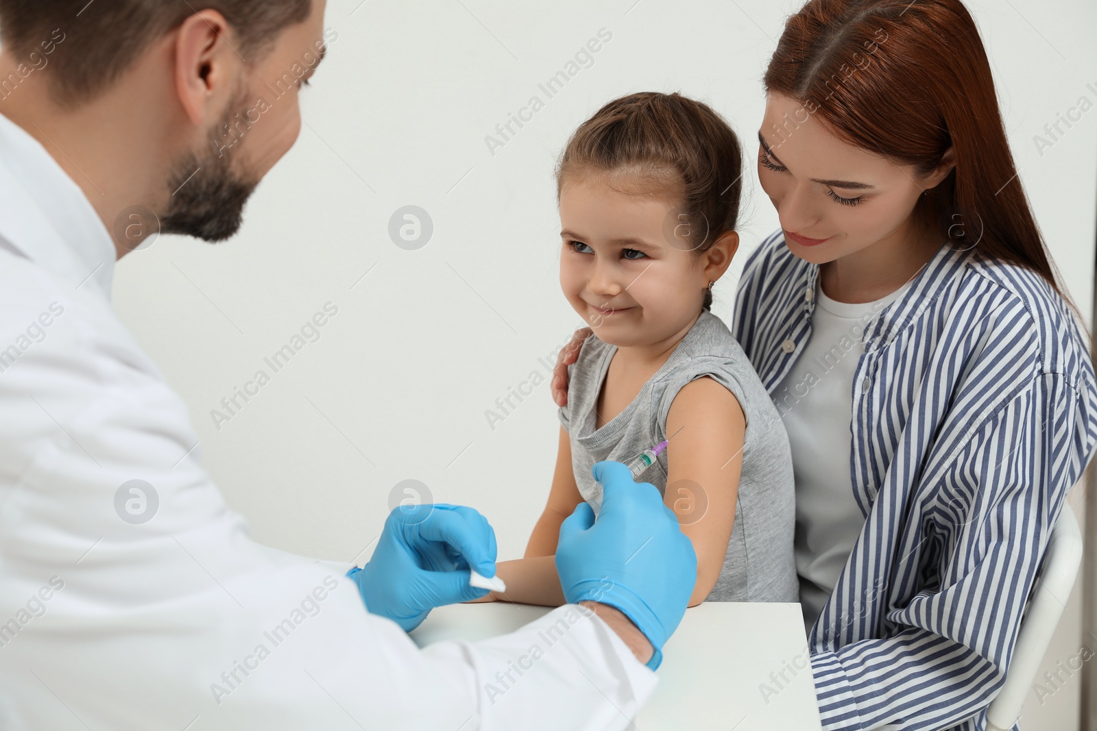 Photo of Children's hepatitis vaccination. Mother with her daughter in clinic. Doctor giving injection to little girl