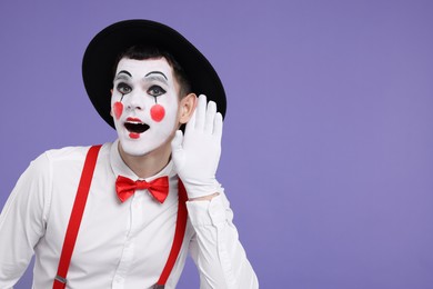 Photo of Funny mime artist showing hand to ear gesture on purple background. Space for text