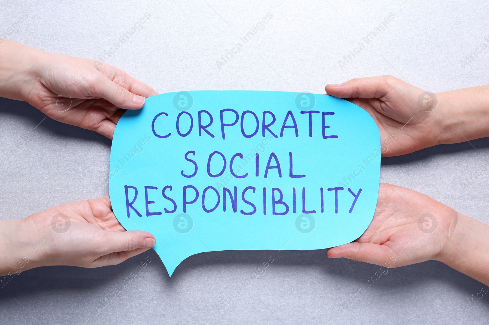 Photo of People holding speech balloon with phrase Corporate Social Responsibility on light grey background, top view