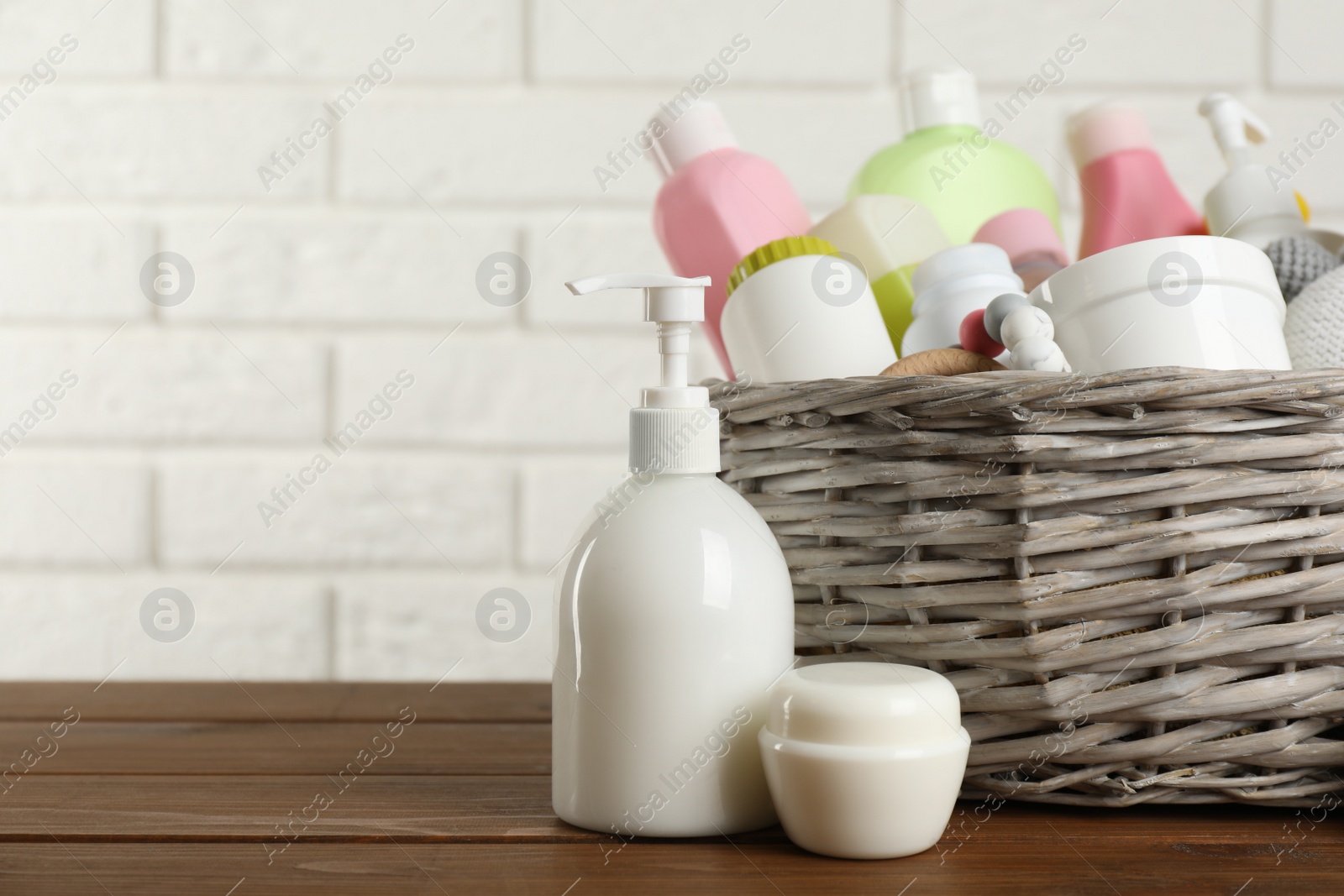 Photo of Wicker basket with different baby cosmetic products and toy on wooden table. Space for text