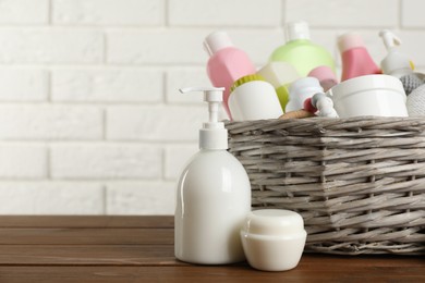 Photo of Wicker basket with different baby cosmetic products and toy on wooden table. Space for text