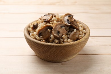 Photo of Delicious pearl barley with mushrooms in bowl on wooden table, closeup