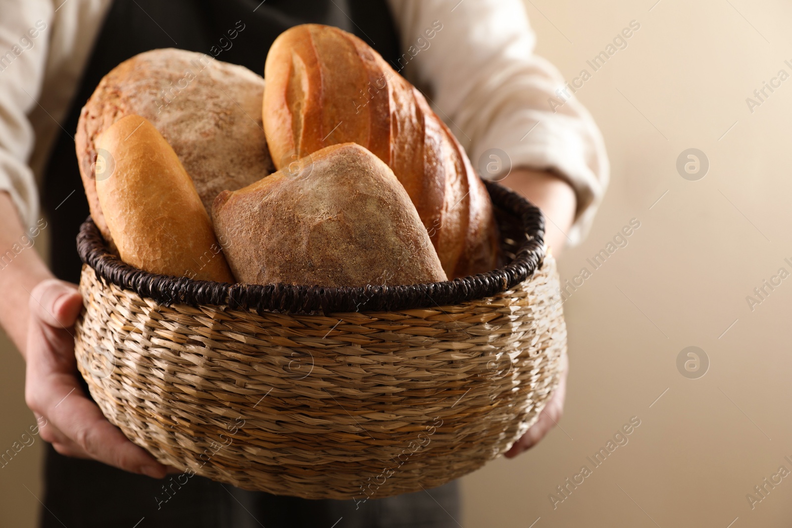 Photo of Man holding wicker basket with different types of bread on beige background, closeup