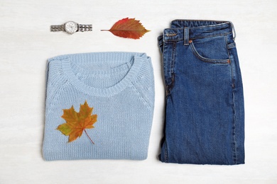 Photo of Stylish outfit and autumn leaves on white wooden background, flat lay. Trendy warm clothes