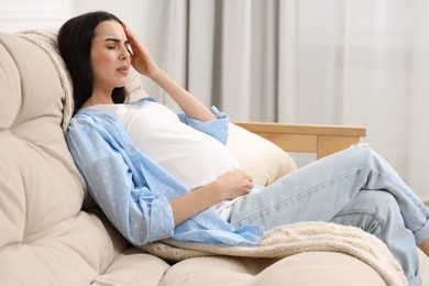 Photo of Pregnant woman suffering from headache on sofa at home