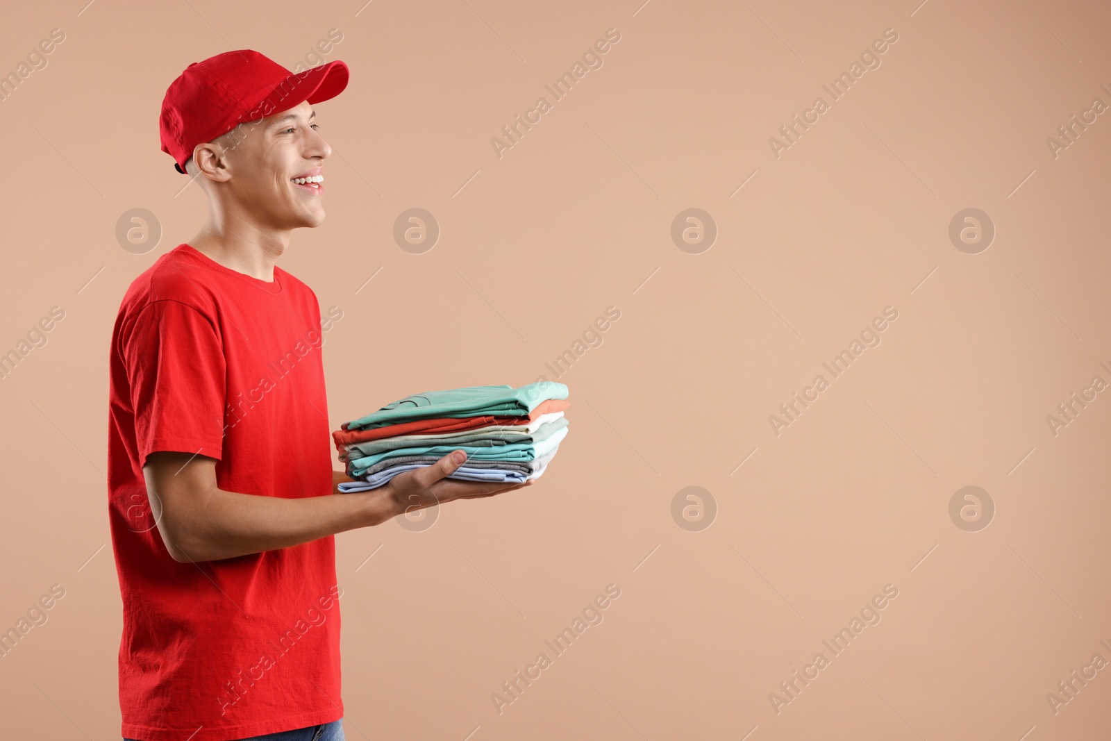 Photo of Dry-cleaning delivery. Happy courier holding folded clothes on beige background. Space for text