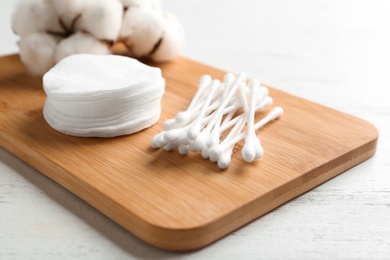 Board with cotton swabs, pads and flowers on white wooden background