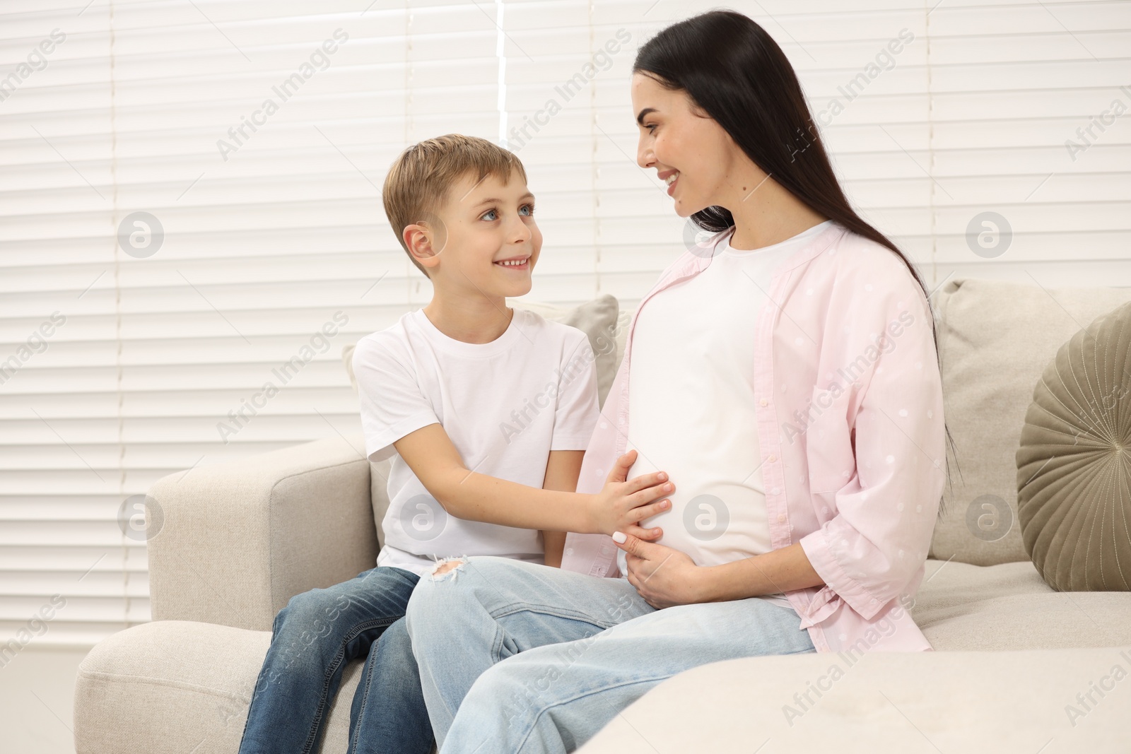 Photo of Cute boy touching pregnant mother's belly at home