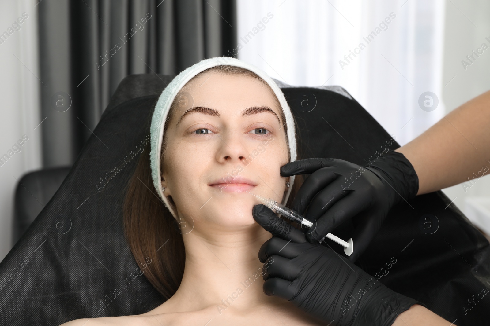 Photo of Cosmetologist giving lips injection to patient in clinic, closeup. Cosmetic surgery