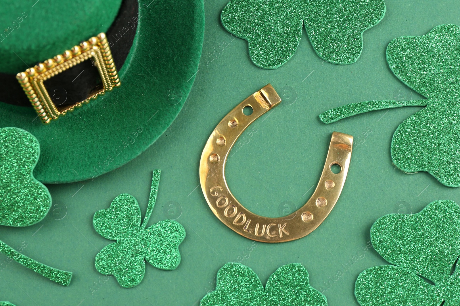 Photo of St. Patrick's day. Leprechaun hat, golden horseshoe and decorative clover leaves on green background, above view